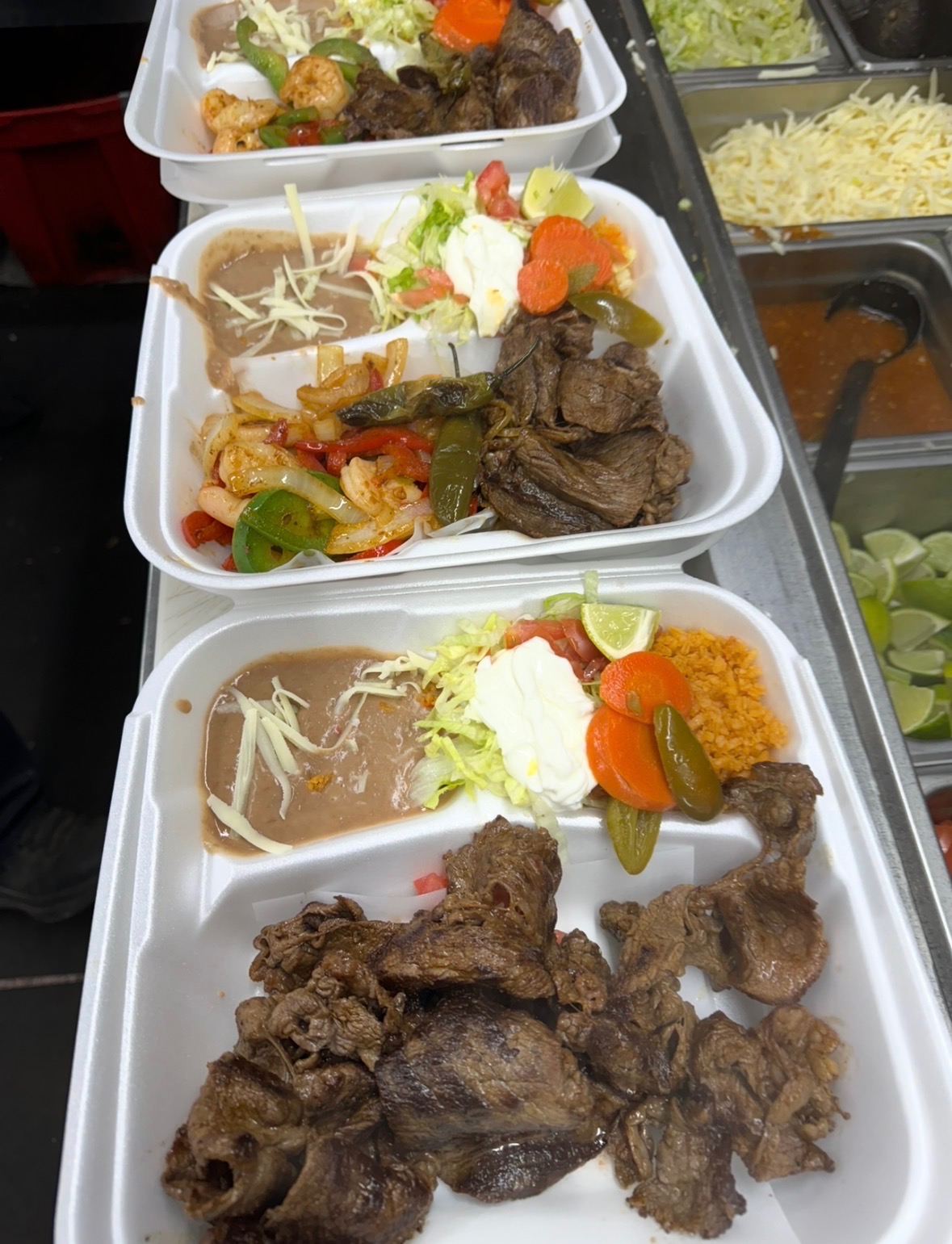 Carne asada plates with rice, beans, lettuce, and sour cream lined up on the prep line